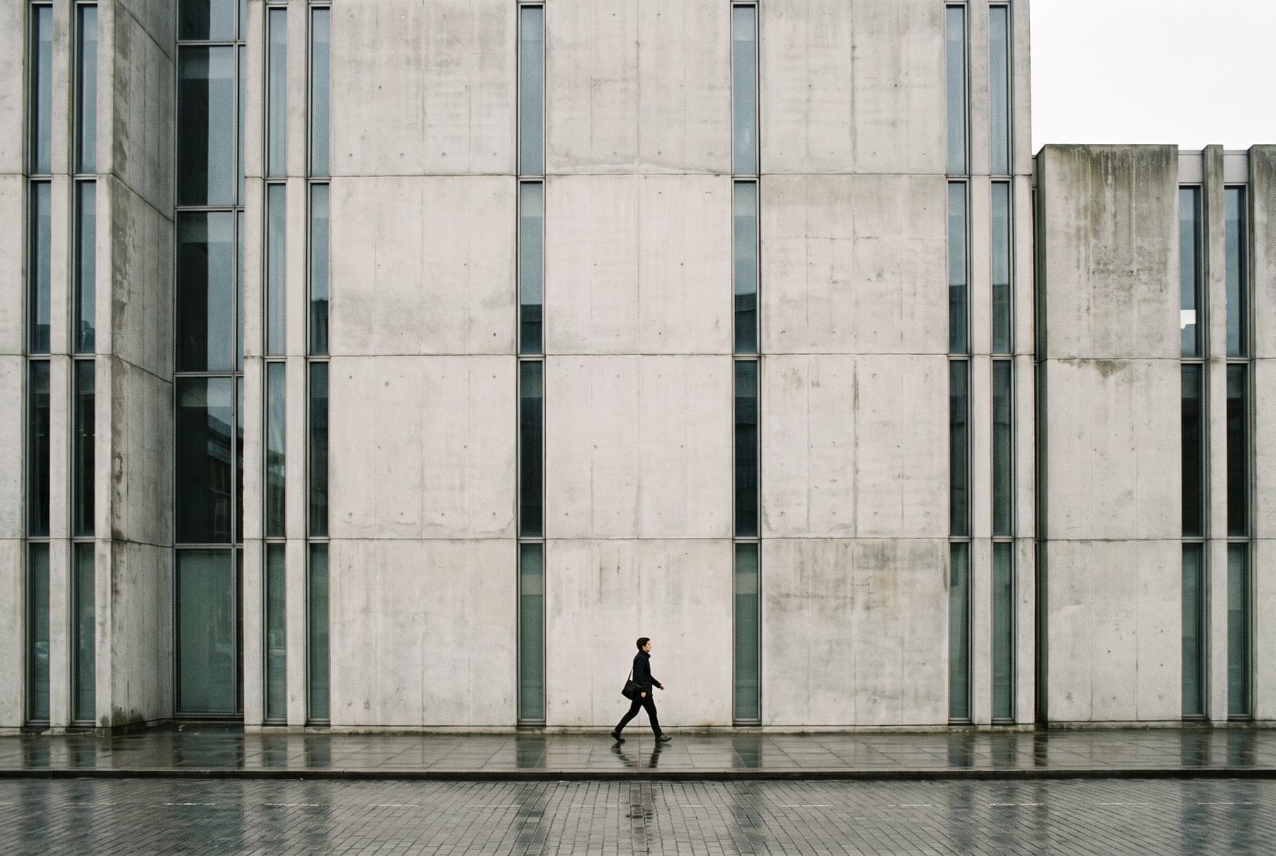 Façade contemporaine en béton et verre, un passant en contrebas